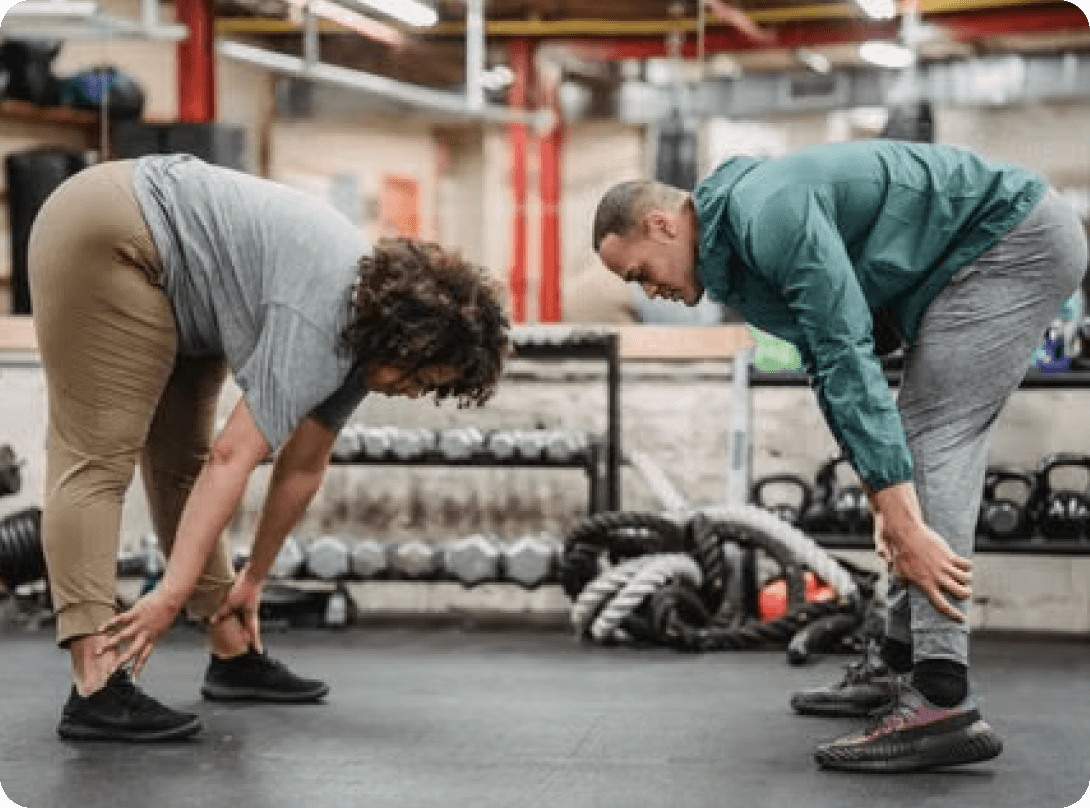 Two adults stretching their hamstrings in a gym
